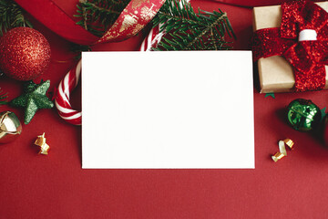 Christmas card mock up. Modern greeting card composition with christmas decorations and gift on red background. Empty postcard template with space for text. Happy Holidays!