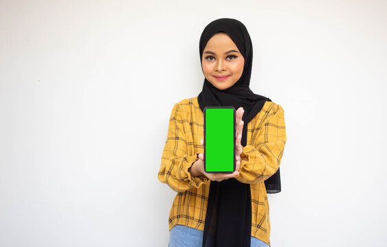 Portrait of cheerful young Asian woman showing mobile phone green screen, isolated on white background
