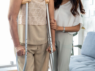 Person helping, female's hand hold the arms of an elderly woman trying to walk on crutches standing...