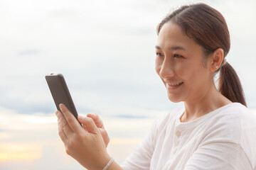 Asian women take photos and video calls at sea and beach in the morning at sunrise with their mobile phones, smartphones for posting to the internet online while traveling on vacation.