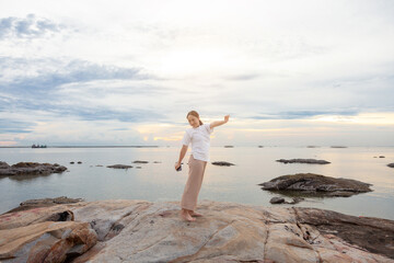 Fototapeta na wymiar Asia woman with smart phones relaxing and arm up on beach. woman stretch relax breathe fresh air. Happy traveler asian woman relieve negative emotions enjoying lazy morning, having peaceful weekend.