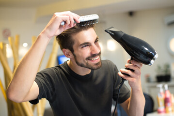 Young man hairdresser drying and combing his own hair in his hair salon - 526526513