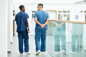 Back view full length of two doctors wearing blue uniform walking in hall of modern clinic, copy...