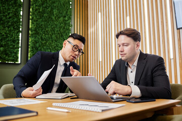 Portrait of two business professionals discussing strategies in meeting and using laptop