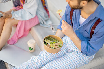 Stylish colleagues eat healthy take away food from a bowl during a lunch time outdoors. Concept of...