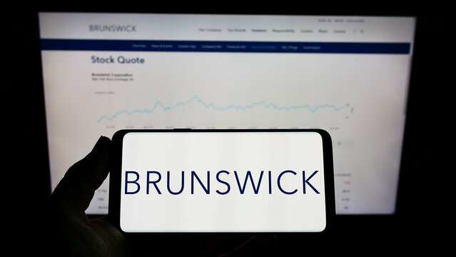 Stuttgart, Germany - 12-12-2021: Person holding mobile phone with logo of American company Brunswick Corporation on screen in front of business web page. Focus on phone display.
