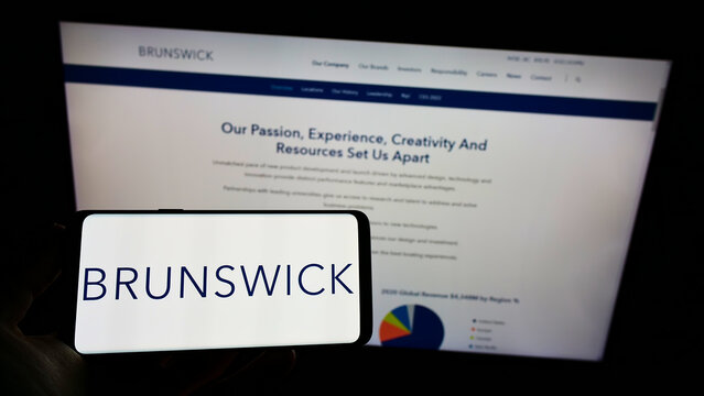 Stuttgart, Germany - 12-12-2021: Person holding cellphone with logo of US boating company Brunswick Corporation on screen in front of business webpage. Focus on phone display.
