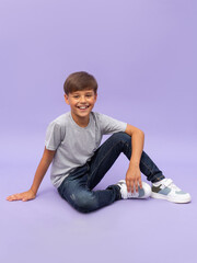 Portrait of young boy sitting isolated over a lilac background