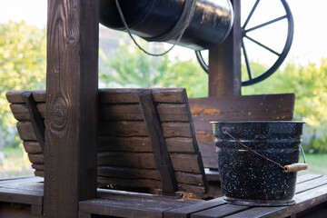 rural wooden well and black bucket of water