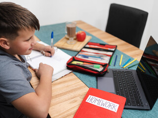 Left handed schoolboy doing homework while using his laptop. Technological concept