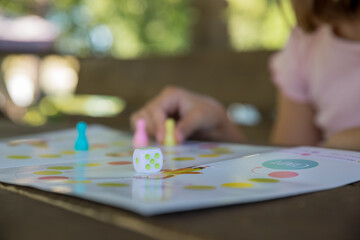 Board game and kids leisure concept - little girl hold figure in hand. yellow, blue, pink chips in children play.Table game. Movement. The girl moves the chip. Victory.