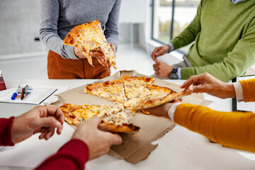 Close up of the businesspeople taking slices of pizza at the office.