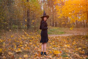 woman in witch costume with broom walking on covered with falling autumn leaves Halloween day forest