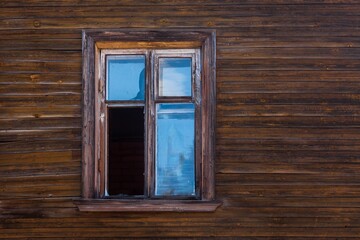 Old window with a wooden frame on the wall of an old yellow wooden house