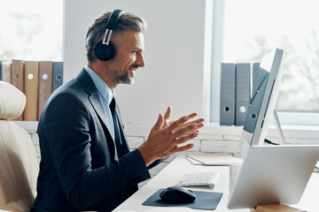 Fototapeta Happy businessman in headphones having web conference while sitting at his working place obraz