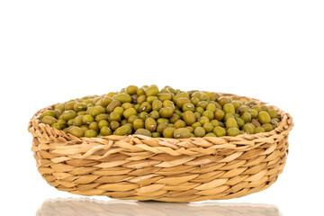 Lots of organic uncooked mung beans in straw bowl, close up, isolated on white background.