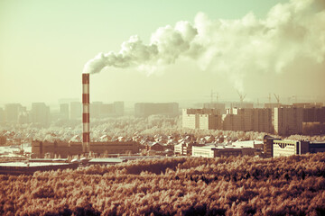 Factory chimney with smoke over winter city with houses in snow