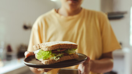 Hand people hold a delicious sandwich with bologna sausage, a plate, fried egg, and lettuce. © PhotoJuthamat
