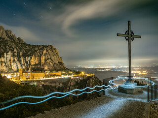 Paisaje nocturno de la montaña de Montserrat con fondo iluminado de poblaciones en Cataluña (España).