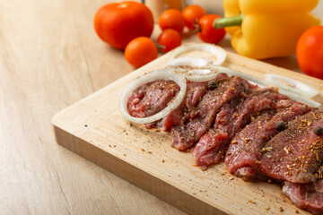 Raw beef with onions marinated with spices and vegetables on a light texture background.Recipe for cooking meat.Juicy steak on a bamboo board, close-up. Place for text, space for copy.
