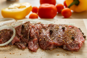 Raw beef with onions marinated with spices and vegetables on a light texture background.Recipe for cooking meat.Juicy steak on a bamboo board, close-up. Place for text, space for copy.