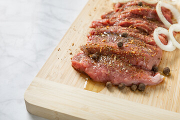 Raw beef with onions marinated with spices on light texture background.Meat cooking recipe.Juicy steak on a bamboo board, close-up. Place for text, space for copy.