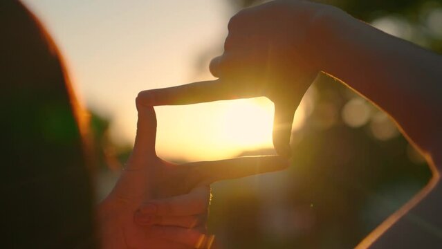 Ambitions Girl shows her fingers frame symbol, sun, Sees like in movies. Hands of young female director cameraman making frame gesture at sunset in park. Seeing world as different. Business planning