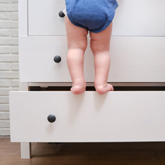 Toddler baby climbed up on the open chest of drawers. Child boy stood on a tall drawer of a white...
