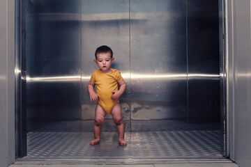 Toddler baby boy stands alone in the elevator of a residential building. A child in an elevator with the doors open. Kid age one year © Андрей Журавлев