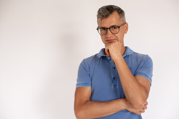 Concentrated mature man wearing glasses looking at camera. Portrait of Caucasian man wearing blue T-shirt standing and looking at camera against white background. Confidence concept
