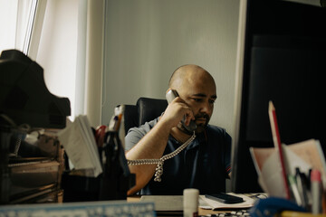 An office worker is talking on a wired telephone. A man uses a wired telephone to make a call