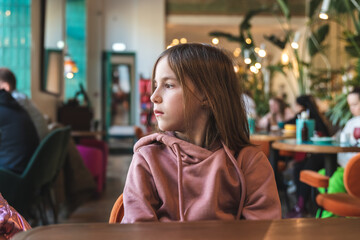 a cute brooding girl sits at a table in a cafe and looks out the window