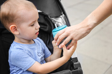 mother gives a child 2 years old to drink water from a baby bottle with a straw in a stroller