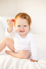 Fototapeta premium A cute red-haired baby girl eats raspberries, drinks water. Children's food. Light background. Space for text. Lifestyle