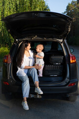 Car journey. Travel with a child by car. Mother and daughter sit in a car with an open trunk