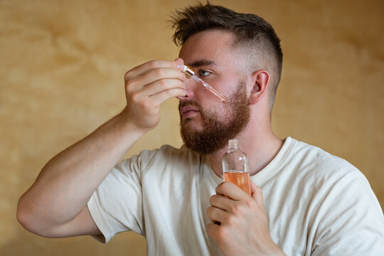 Portrait brutal handsome bearded man holding glass bottle with medicine, minoxidil, serum, oil for hair and beard growth dark brown red. Lifestyle people, male personal self care, products, accessory.