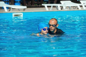 A swimming coach conducts an individual lesson with a little preschool girl, teaches how to swim correctly in the pool water in the warm season