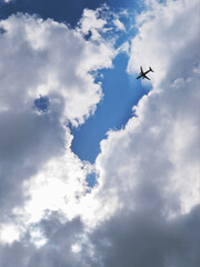 The passenger airplane is flying far away in the blue sky and clouds. Dramatic clouds with the sun shining through them. Aircraft in the air. Vertical illustration. Passenger air transportation