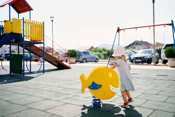 Little girl in a panama stands next to a spring swing. High quality photo