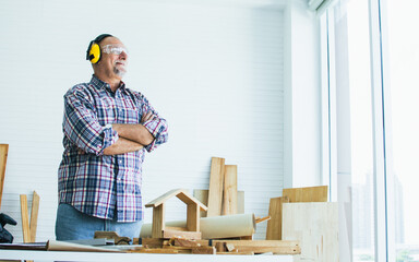 Senior Caucasian retired old male woodworker, carpenter looking out window, wearing check shirt,...