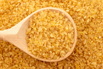 Bulgur wheat background. Bulgur grains lie in a wooden spoon. View from above
