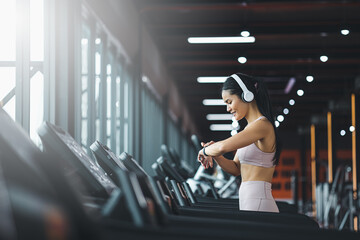 Happy beautiful young asian woman running on treadmill and listening to music via headphone during...