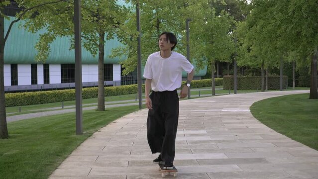 A young attractive Asian man rides a skateboard calmly in the park