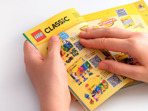 Tambov, Russian Federation - December 21, 2021 A Woman hands opening Lego catalog on a page with Lego Classic sets.