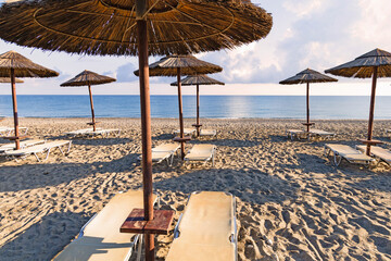 Empty beach with sun loungers and umbrellas in the early morning on a sunny day on the Crete island Greece. . High quality photo