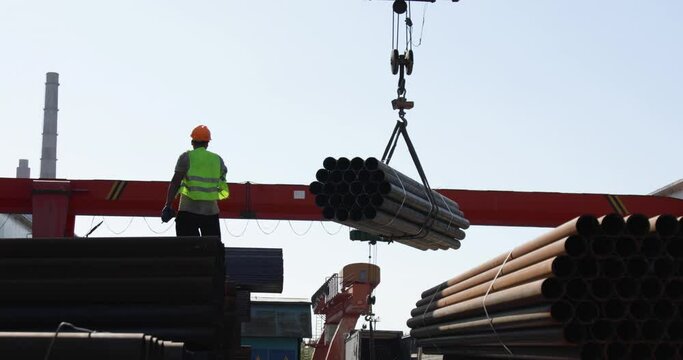 Worker transporting stack of metal pipes with gantry crane