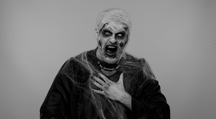 Sinister man in carnival costume of Halloween crazy zombie with bloody wounded scars face pointing...