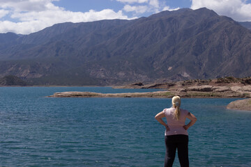 Blonde woman looking a beautiful scenery with a lake and mountains on a cloudy day.