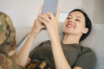 Military woman lies on sofa , holds mobile phone in hands