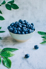 Ripe blueberry in  bowl with green leaves over gray table background copy space.